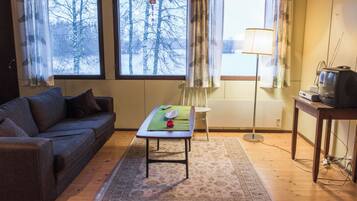 Ein gemütliches Wohnzimmer mit einer Couch, einem kleinen Tisch, einer Lampe und einem Fernseher auf einem Holztisch.