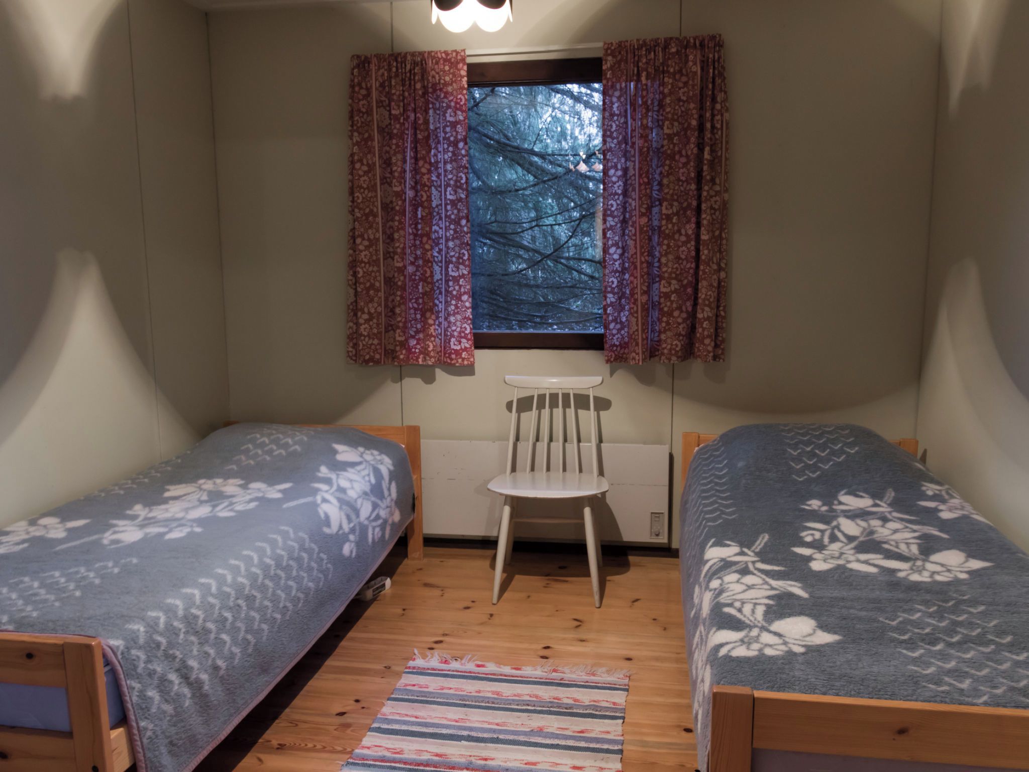 A small, cozy room with two single beds, a chair, and a window with curtains.
