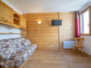 Um quarto aconchegante com sofá estampado, paredes de madeira, TV fixada e janela com cortinas.