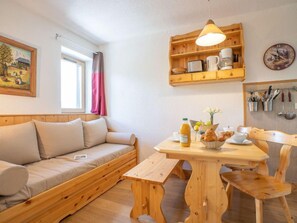 Um quarto aconchegante com um sofá de madeira, uma mesa de jantar de madeira com cadeiras, uma luminária pendente, um relógio de parede e uma janela com cortinas.