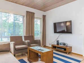 A living room with a sofa, two armchairs, a coffee table, a flat-screen TV, and a wooden entertainment unit with a radio.