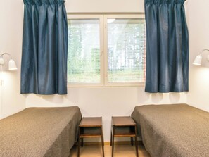 Une chambre avec deux lits simples, une fenêtre avec des stores et deux lampes de chevet.