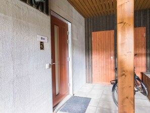 L’entrée d’un hôtel, avec une porte en bois, une plaque indiquant le numéro, et un vélo garé à l’extérieur.