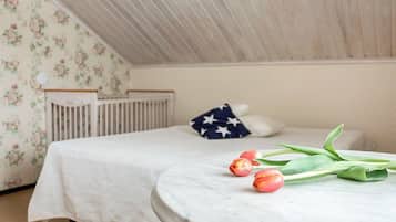 A bedroom with a bed, a crib, a round table with tulips, and a wall with floral wallpaper.