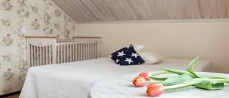 Ett sovrum med en säng, en spjälsäng, ett runt bord med tulpaner och en vägg med blommig tapet.