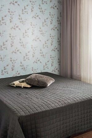 Ein Bett mit einer gesteppten, grauen Tagesdecke und einem gemusterten Kopfkissen.