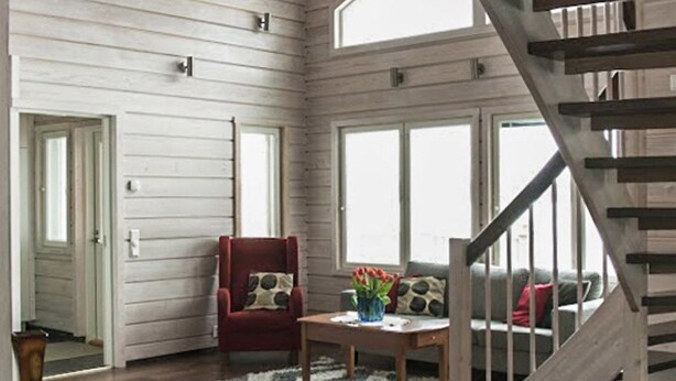 Ein geräumiges Zimmer mit Holzboden, einem roten Sessel, einer Couch, einem Tisch mit Blumen und einer Treppe.
