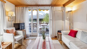 Ein gemütliches Wohnzimmer mit Holzbalkendecke, einer Couch, einem Couchtisch und einem Fernseher.