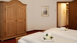 Quarto de hotel com duas camas, um guarda-roupa de madeira, um quadro na parede e uma porta que dá para outro cômodo.