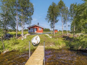 A cabin with a dock leading to a small boat, surrounded by trees and a clear stream. - Ruka-kitkan käki by Interhome (Kuusamo)