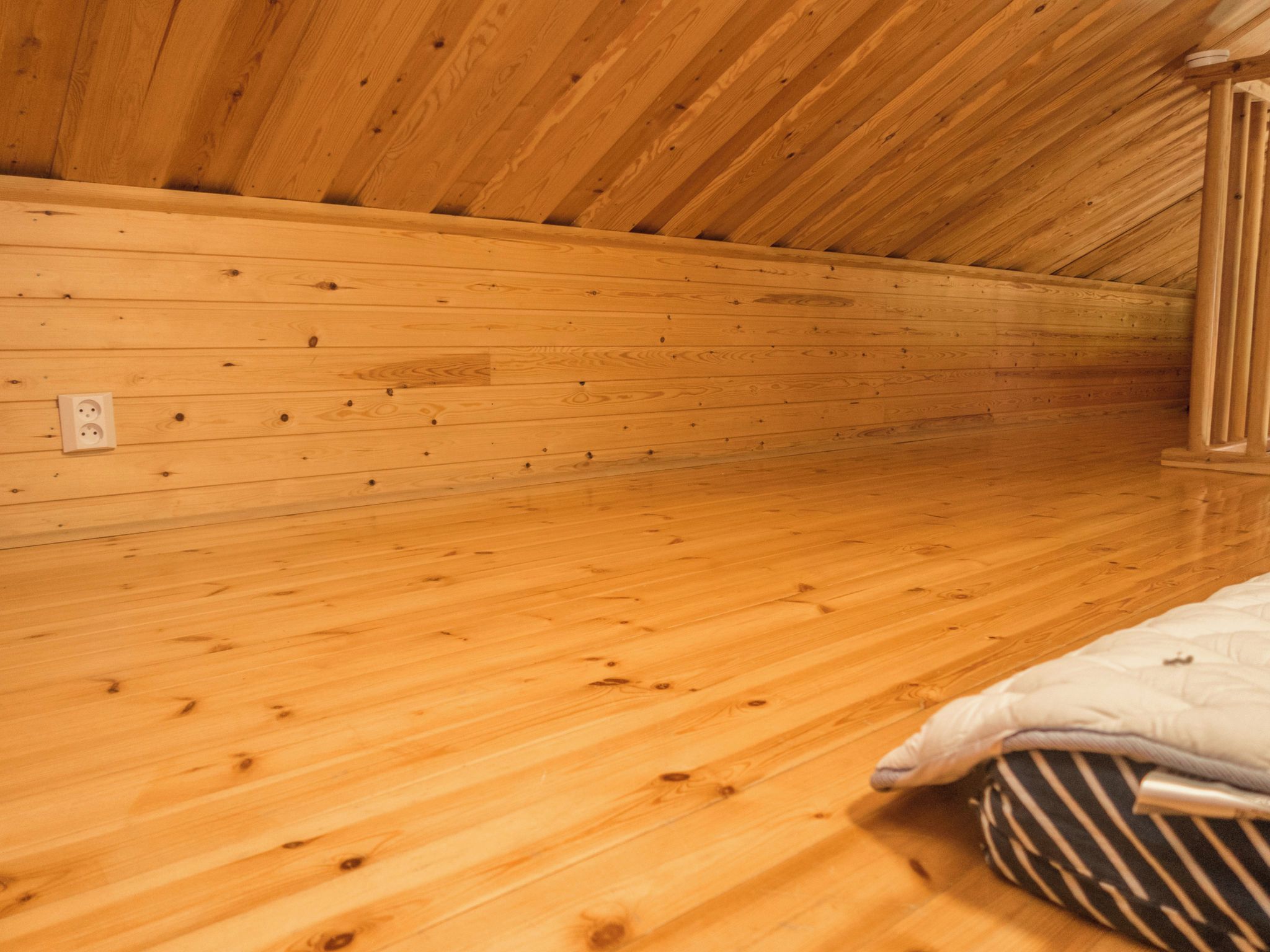Una habitación con paredes y suelo de madera, una cama con ropa de cama a rayas y un enchufe en la pared.
