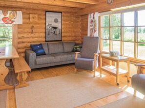 A cozy cabin interior with a wooden interior, a gray sofa, a chair, a small table, and a window with a view of greenery. - Ruka-kitkan käki by Interhome (Kuusamo)