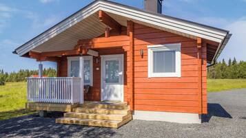 Une petite cabane en bois, de plain-pied, avec une véranda, une cheminée et une allée gravillonnée.