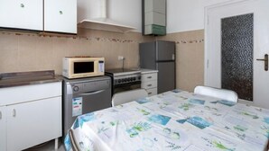 A compact kitchen with a microwave, stove, refrigerator, and a bed with a floral bedspread.