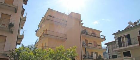 Un immeuble résidentiel à plusieurs étages, doté de balcons, avec un ciel dégagé et une clôture au premier plan.