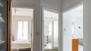 A spacious, well-lit room with a bed, a small table, and a door leading to another room.