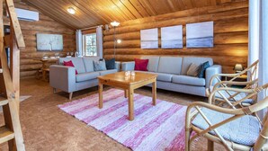 Accogliente interno di una baita di legno con soffitto in legno, un divano, un tavolo da pranzo e una grande finestra.