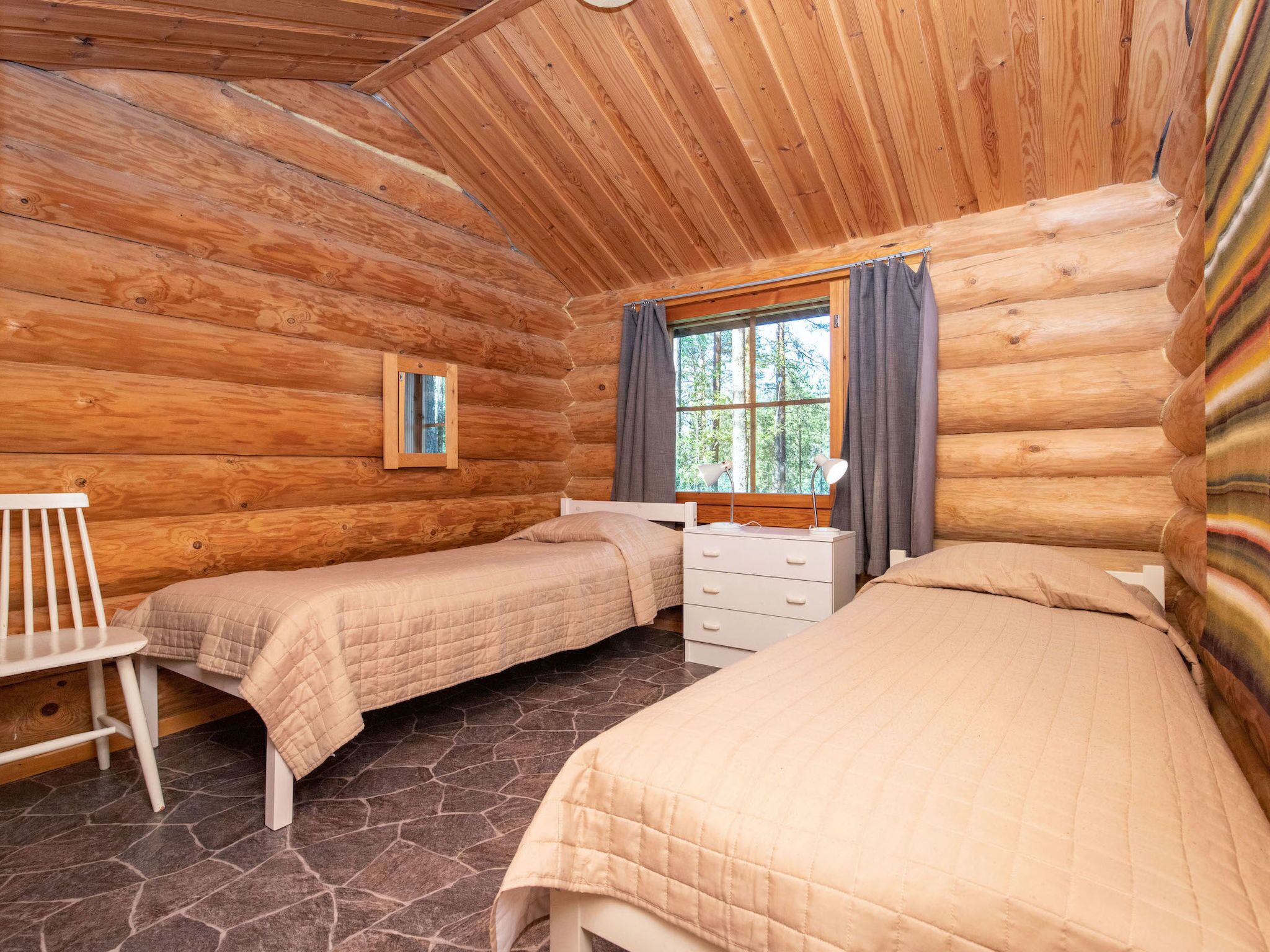 Un dormitorio de cabaña de madera con dos camas, un escritorio pequeño y una silla.