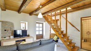 A modern living room with a wooden staircase, a television, and a stone wall.