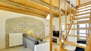 A modern living room with a stone wall, a white sofa, a television, and a wooden staircase.