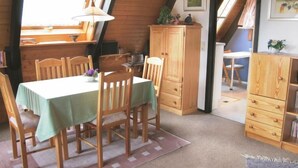 Et hyggeligt spiseomr åde med et bord dækket til fire personer, træstole, et skab og en trappe til et andet rum.
