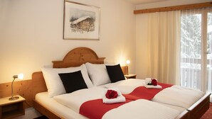 Une chambre d’hôtel avec un grand lit, deux tables de chevet, une petite table, un tableau encadré au mur et une fenêtre avec des rideaux.