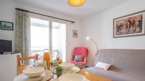 Un salon confortable avec un canapé, une table à manger avec des bols et des verres, un téléviseur et un balcon offrant une belle vue.