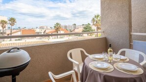 Un balcon avec une table dressée pour deux personnes, un barbecue et une vue sur les immeubles et les palmiers.