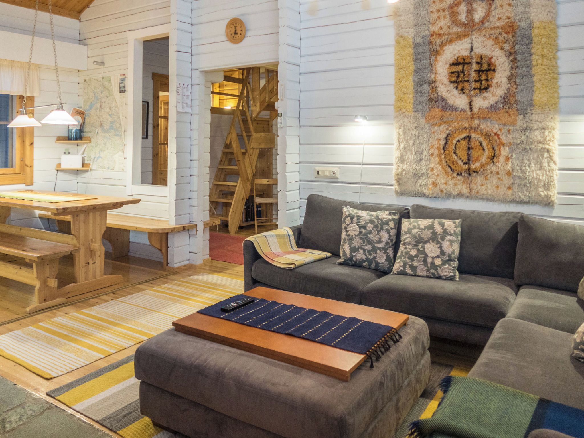 A cozy living room with a sofa, ottoman, and a coffee table. There is a wooden table and chairs in the background.