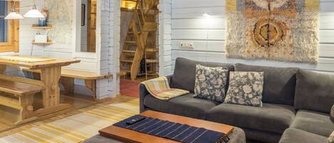 A cozy living room with a sofa, ottoman, and a coffee table. There is a wooden table and chairs in the background.