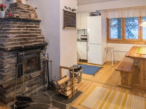 A cozy kitchen with a stone fireplace, a wooden table, and a view of the outdoors through a window. - Purnukylä 4 by Interhome (Kuusamo)