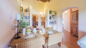 A dining area with a wooden table set for four, surrounded by wicker chairs, and a bookshelf filled with books.