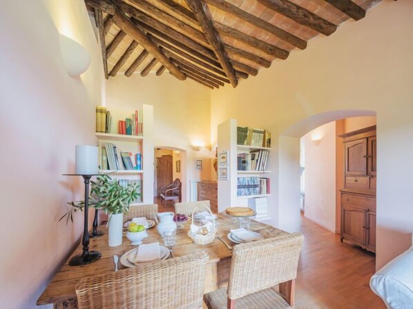 A dining area with a wooden table set for four, surrounded by wicker chairs, and a bookshelf filled with books.