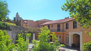 A courtyard with a stone wall, a small table with chairs, and a building with a tiled roof and arched windows.