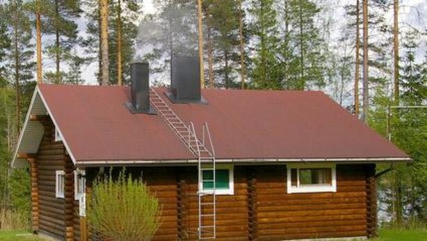 A log cabin with a red roof, a chimney, and a ladder leading to the roof. - Kettupirtti by Interhome (Juva)