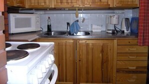 A kitchen with wooden cabinets, a white stove, a microwave, and a sink. - Kettupirtti by Interhome (Juva)