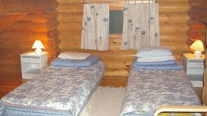 A log cabin room with two beds, each with a lamp, a window with curtains, and a wooden wall. - Kettupirtti by Interhome (Juva)