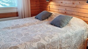 Un lit avec une couvre-lit à motifs, deux oreillers, une lampe de chevet et des panneaux de bois au mur.