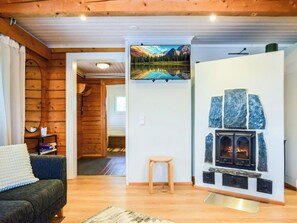 A cozy room with a fireplace, wooden walls, a sofa, and a painting of a mountain landscape.