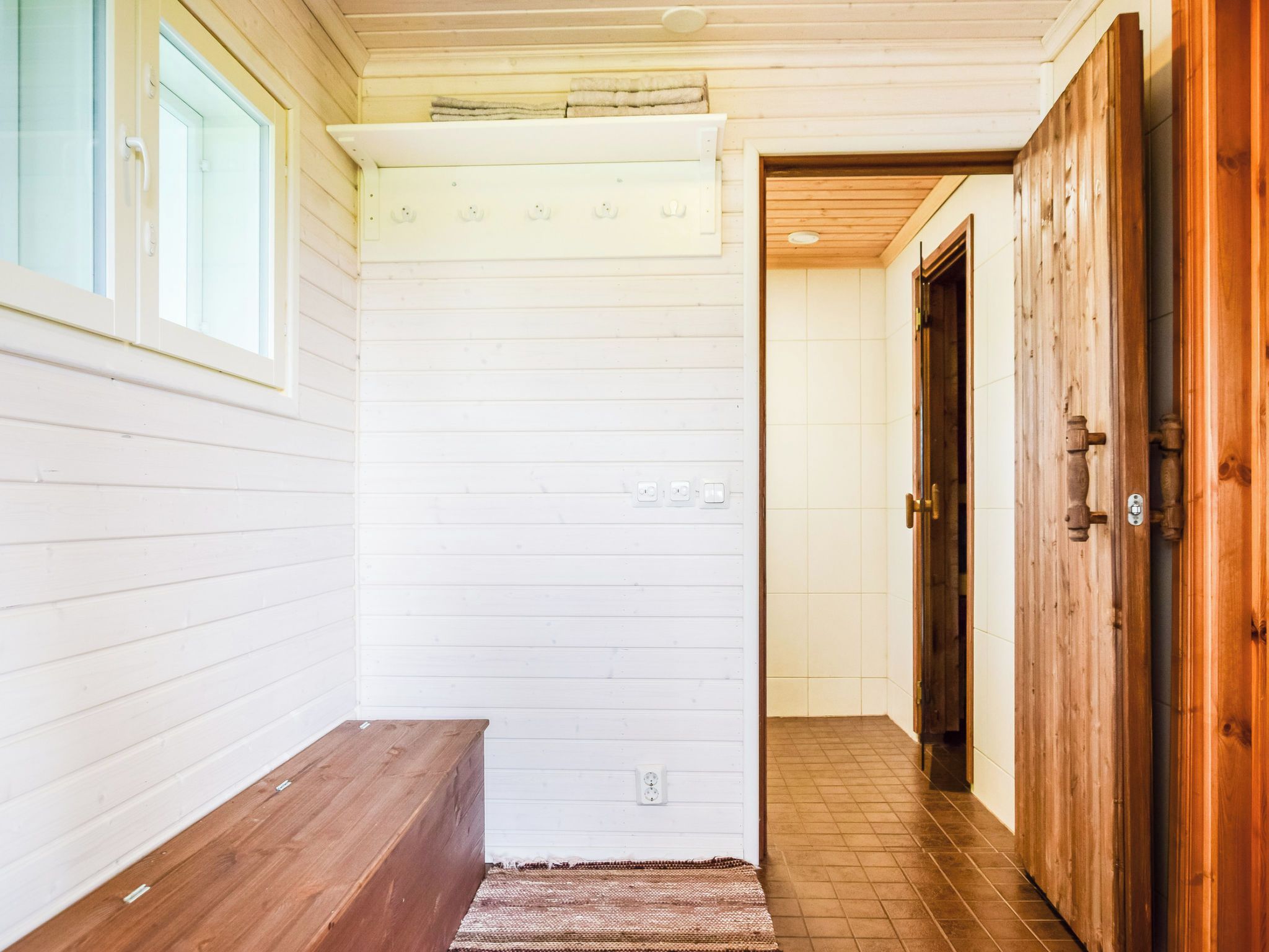 Un couloir avec un banc en bois, un mur blanc doté de prises électriques et une porte en bois.