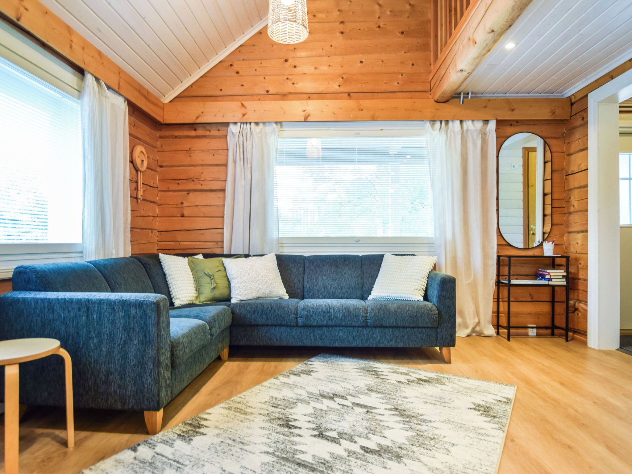 A cozy living room with a sectional sofa, a small round table, a mirror, and a bookshelf.