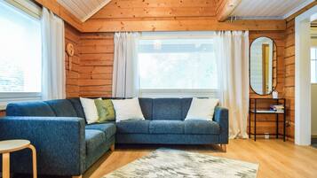A cozy living room with a sectional sofa, a small round table, a mirror, and a bookshelf.