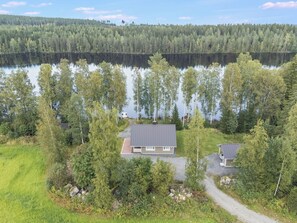 A house with a metal roof, surrounded by trees and a lake.