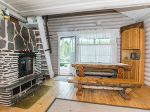 A log cabin interior with a stone fireplace, wooden table, and a door leading outside.