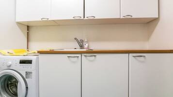 A compact kitchen with a washing machine, a sink, and cabinets.