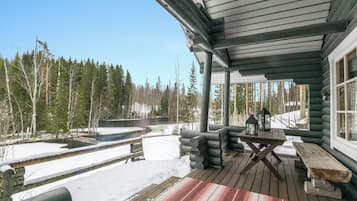 A log cabin with a covered porch, a stone wall, and a view of a snowy forest.