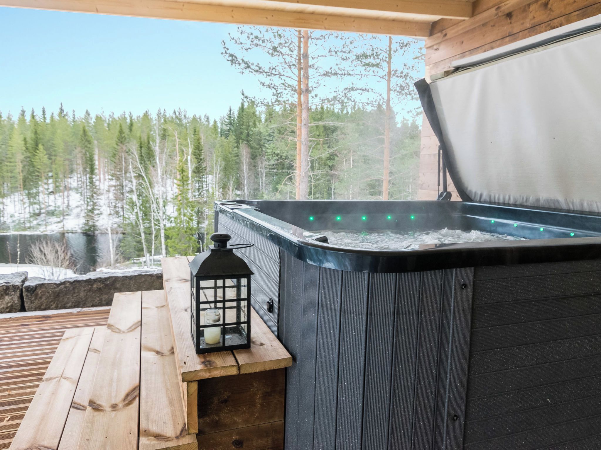 Lämminvesiallas, jossa on puinen terassi ja lyhty, ja jonka ympärillä avautuu metsämaisema.