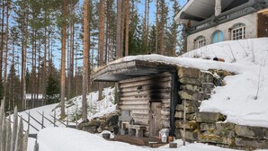Una cabaña rústica con fachada de piedra, terraza de madera y paisaje cubierto de nieve.