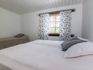 Un dormitorio con cama, ventana con cortinas y un banco.