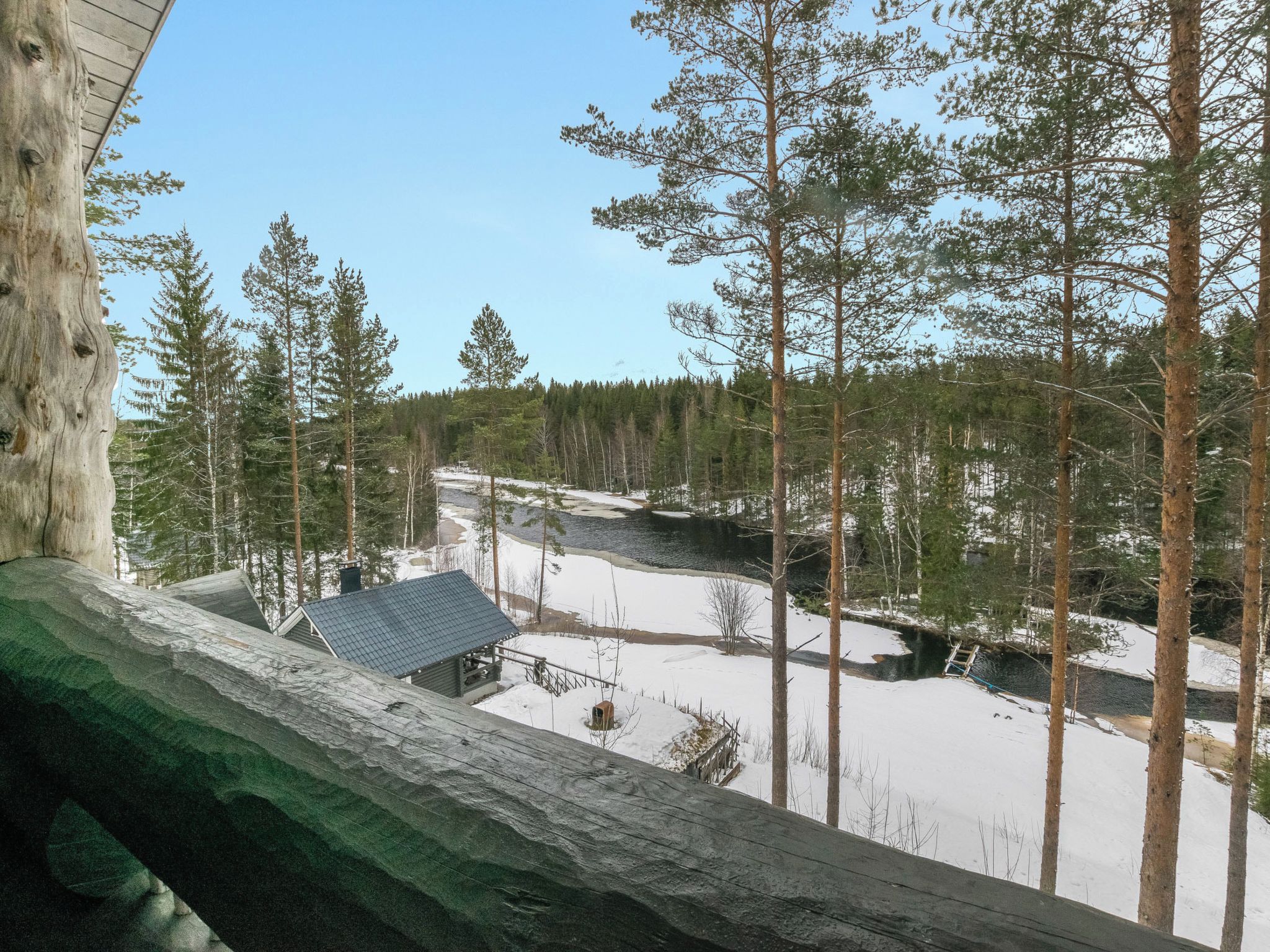 En stuga med ett snötäckt landskap runt omkring, omgiven av höga tallar.